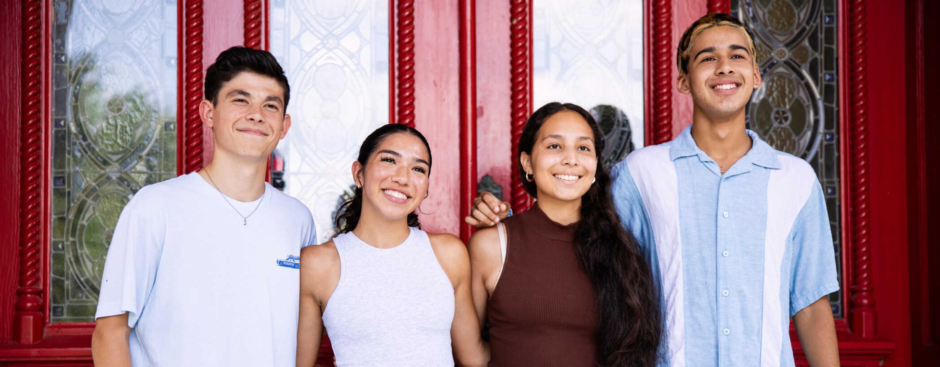 Four students stand together for a group photo at Main Building's red doors after orientation.