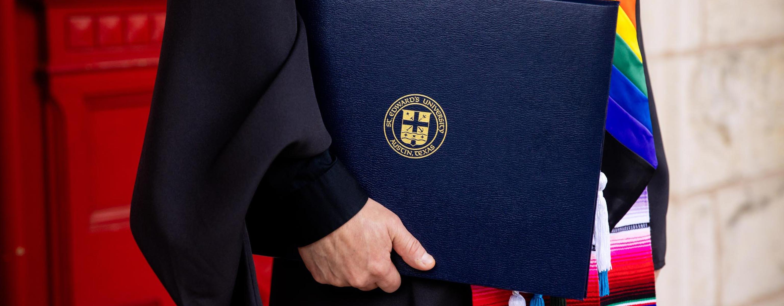 Graduating senior holding their diploma in front of the Red Doors at Main Building.