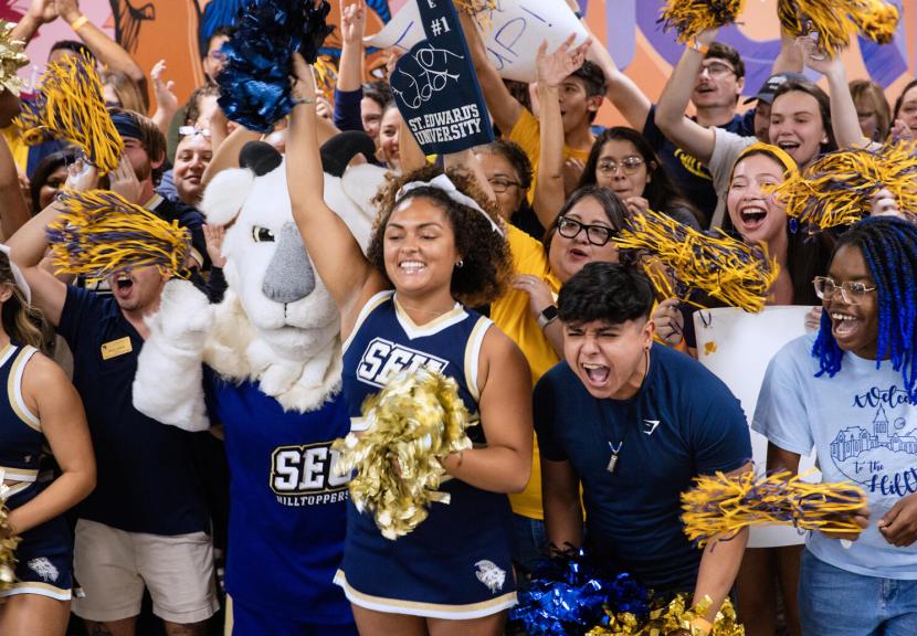 A large crowd of students and a goat mascot dressed in blue and gold cheering with foam fingers and pom poms