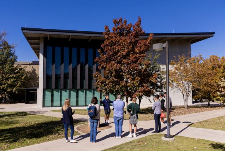 A campus tour guide leads a tour and chats with prospective students and families on a path outside Munday Library.