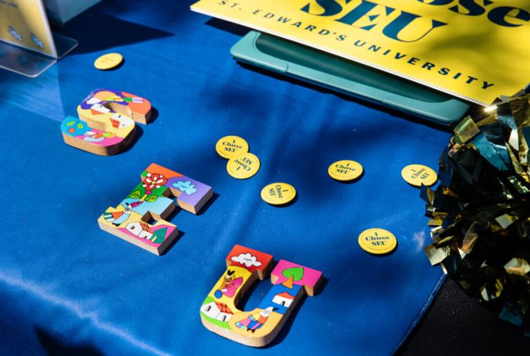 SEU block letters with colorful designs on a blue table cloth with yellow and blue I Chose SEU pins scattered around.