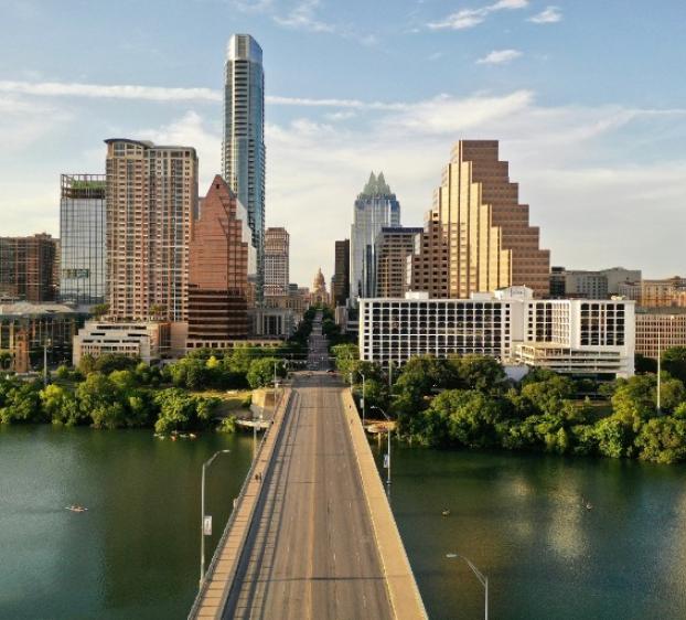 Aerial view of a road bridge over water leading to downtown Austin with tall buildings in the background.