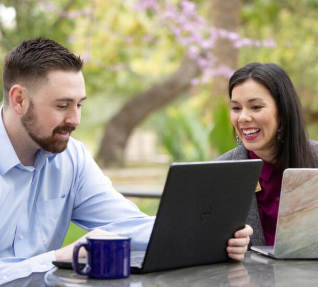 Two people with laptops talk and work outside on a nice day