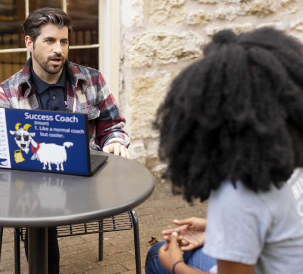 A St. Edward's University success coach talking with a student outside at a table