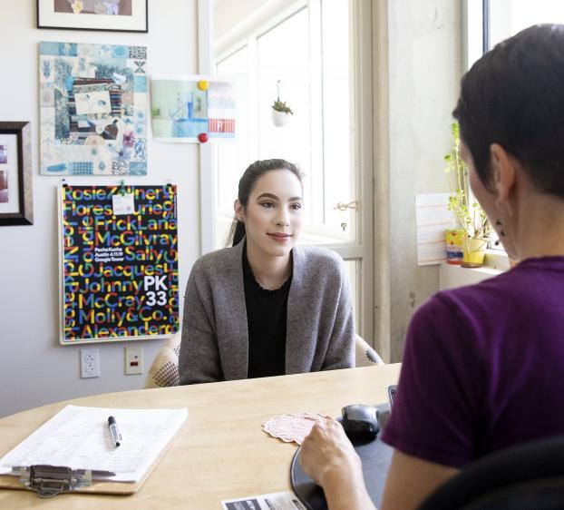 A student sits in an advisor's office and listens during their meeting.