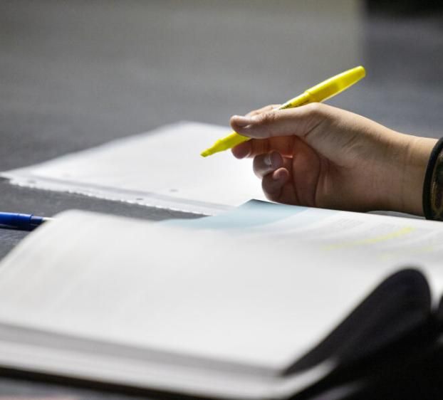 A hand holds a highlighter on top of a notebook at a desk.