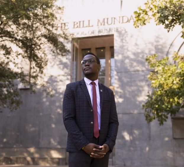 Emmanuel Epau wears a suit and stands outside of The Bill Munday School of Business.