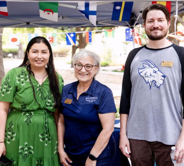 International Student Services staff members stand in front of tent that has mini flags of various countries adorning it.