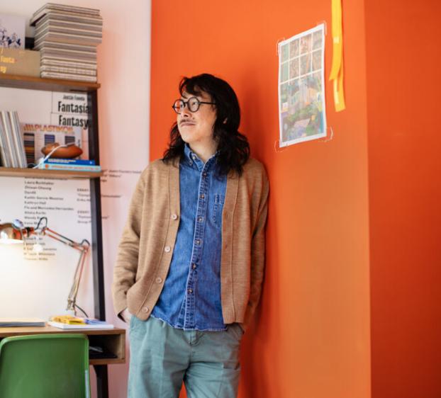 Professor Jimmy Luu leans on an orange wall in his downtown studio.