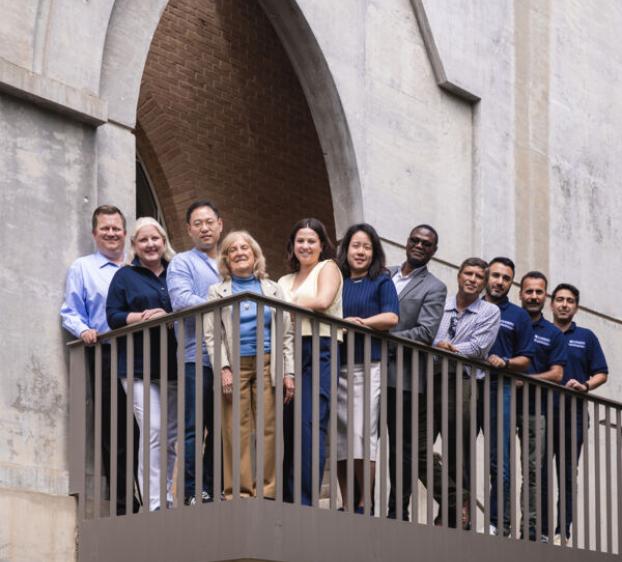 The Bill Munday School of Business faculty and staff stand outside Trustee Hall on the stairway patio.