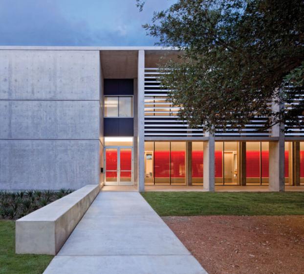 A view of Equity Hall and its courtyard at dusk, with the interior red walls illuminated by the hallway lights.