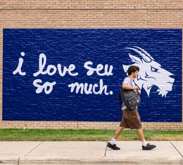 Student walks in front of "i love seu so much" mural