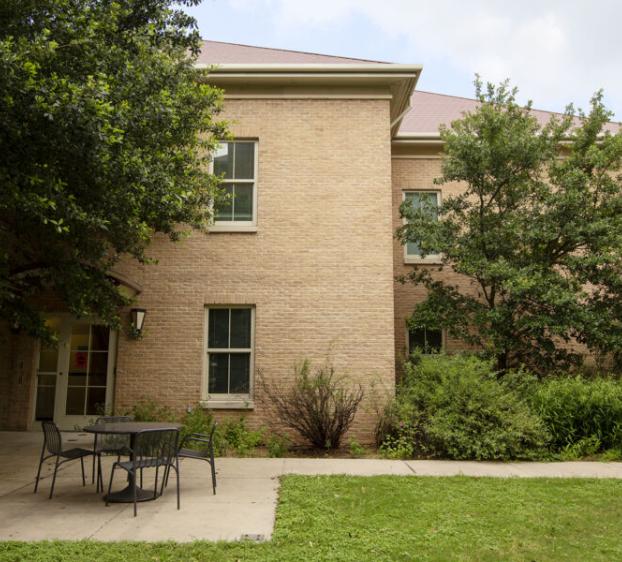 Photo of the outside of Casa. The building is light tan and is surrounded by trees. Chairs and tables are on a concrete patio.