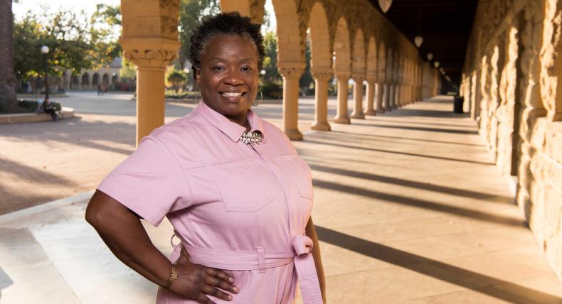 Mona Hick stands in a pink jumpsuit on Stanford's campus.