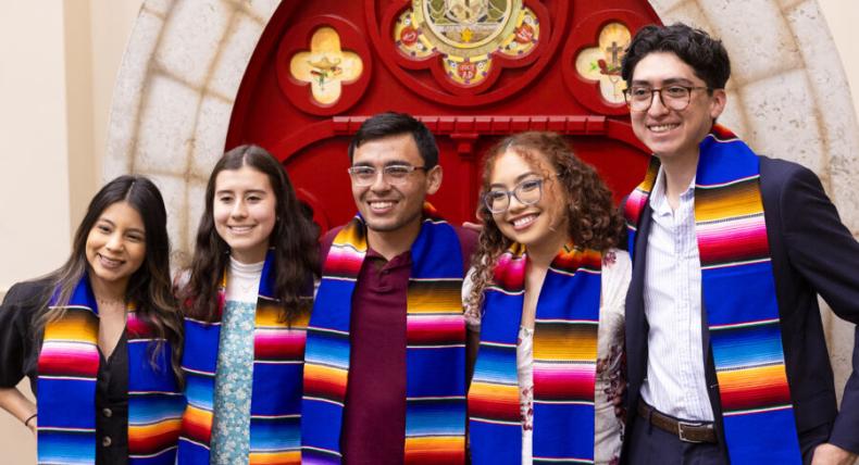 4 students in front of a red door with graduation sashes 