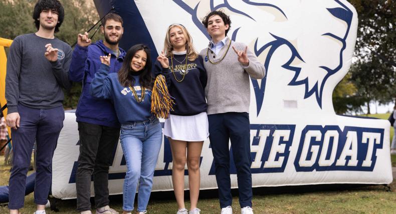 Five students hold up the toppers up hand sign in front of a Fear The Goat inflatable.