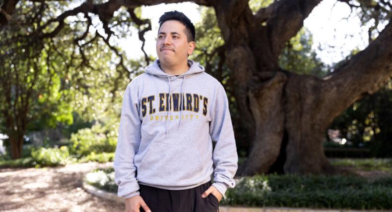 Ethan Tobias wears a St. Edward's hoodie and stands in front of Sorin Oak.