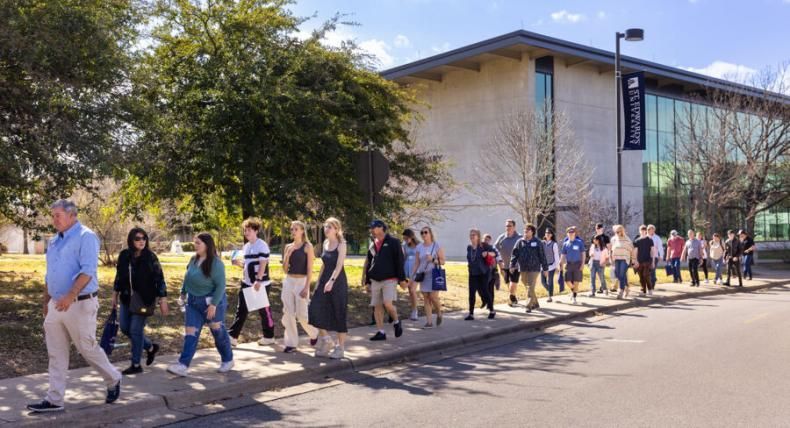 Families participating in a campus tour walk on a sidewalk with Munday Library in the background