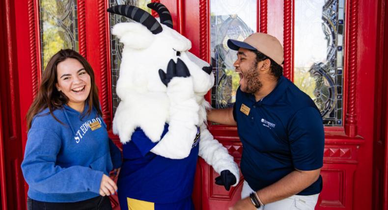 Two students and topper stand and laugh together outside of the red doors.