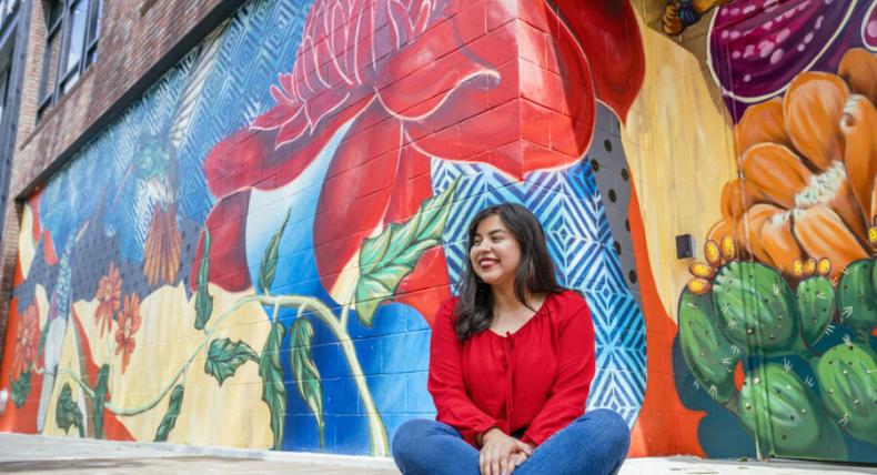 Bianca Esquivel sits in front of a colorful mural.