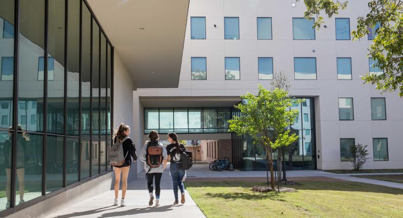 Three students walk on a path by the St. Andre Apartments.