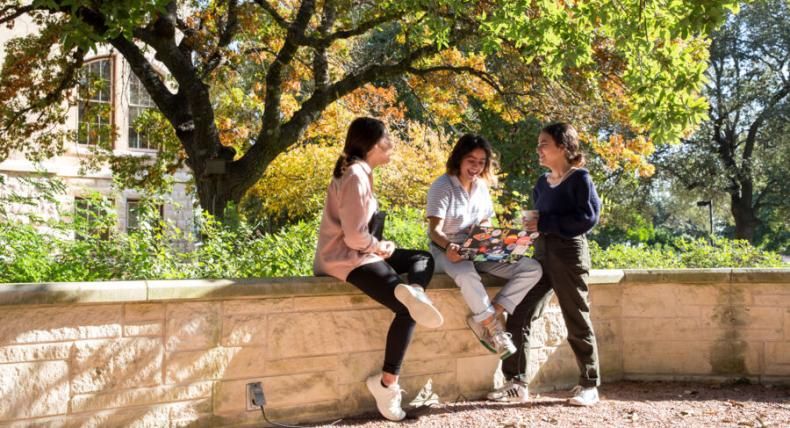 Three students sit on campus gathered around a laptop.