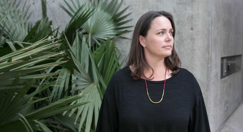 Laurie Cook Heffron stands by tropical greenery and a concrete wall.