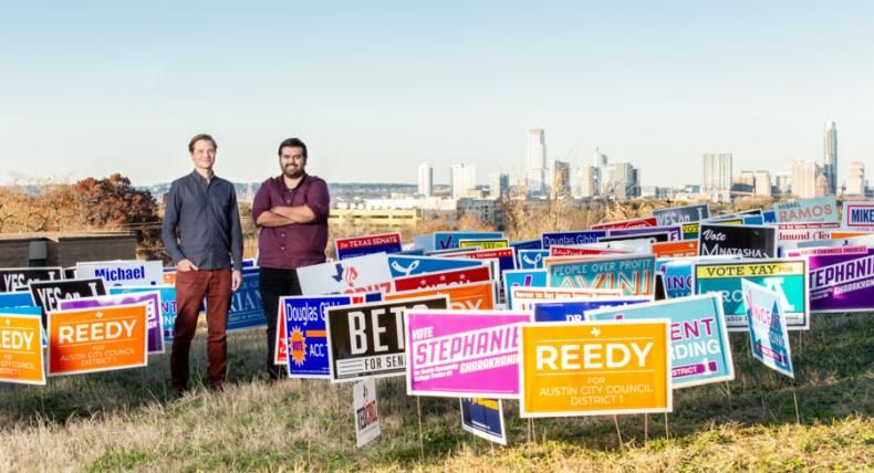 Jason Callahan and Omar Dominguez stand with a lot of candidate election signage with a view of the skyline in the background.