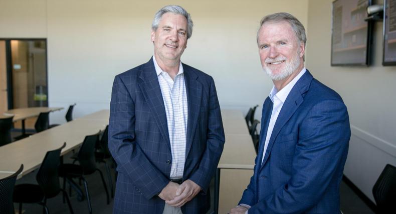 Alumni Steve Shadowen and Bob Hilliard wear blazers and are in a classroom in the Munday Library.