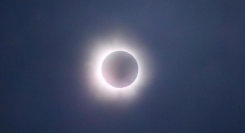 The image captures a solar eclipse in its totality phase, where the moon completely covers the sun, leaving only the bright corona visible as a glowing ring around the darkened disk. The sky appears dark, adding to the dramatic effect of the eclipse. The soft, glowing light of the corona creates a striking contrast against the shadowed moon, making this a captivating depiction of a natural celestial event.