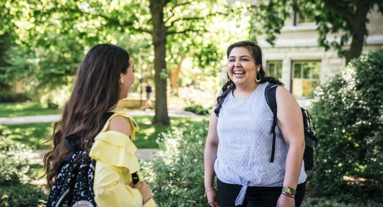 Two students talk outside amongst greenery.