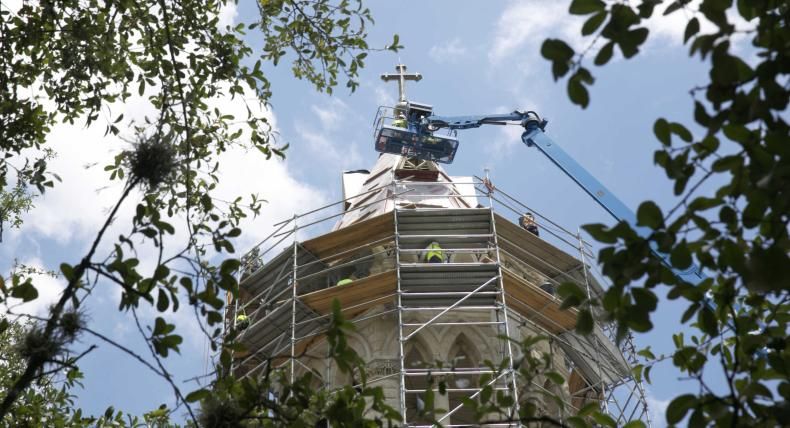 Main Building's steeple under construction, framed by foliage.