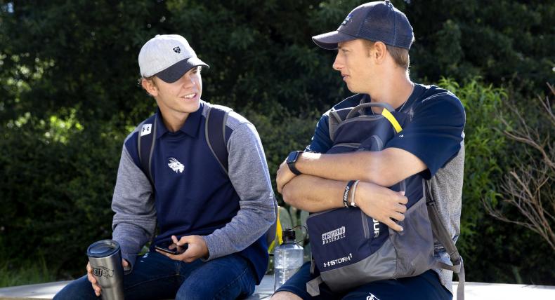 Two students wearing St. Edward's athletic gear sit and chat outside.