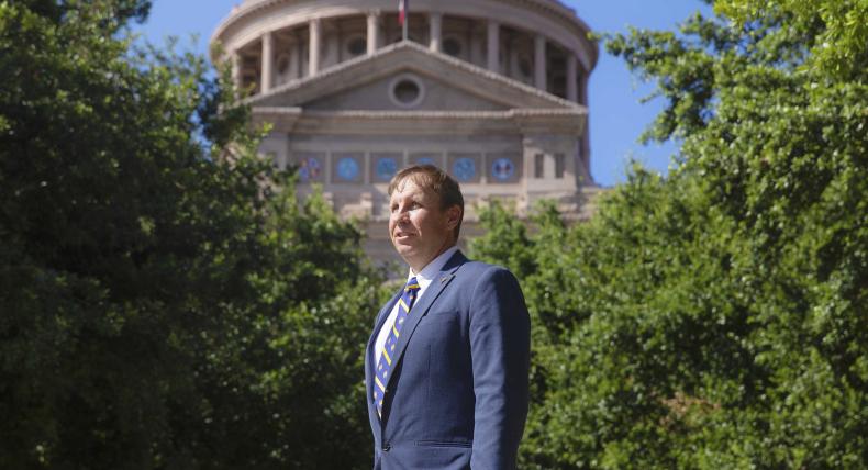 Professor David Thomason stands outside of the Texas State Capitol, framed by trees.