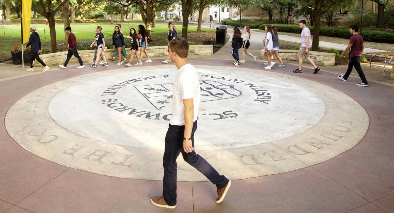 Students walk around the university seal during the Legacy Walk.