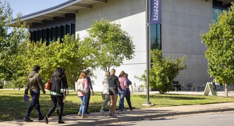 Families walk on a sidewalk in front of Munday Library during a campus tour.