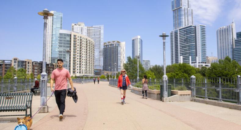 skyline of downtown austin with several people crossing a bridge 