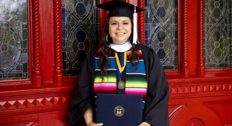 student holding diploma in front of red doors 