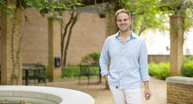 Bailey Galicia stands in the Moody Hall courtyard by a fountain with trees in the background.