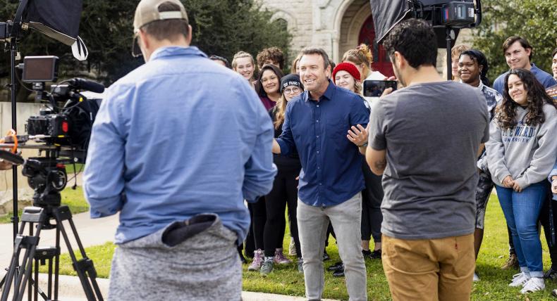 A film crew films Alex Boylan, host of The College Tour, as he speaks in front of a group of students outside of Main Building.