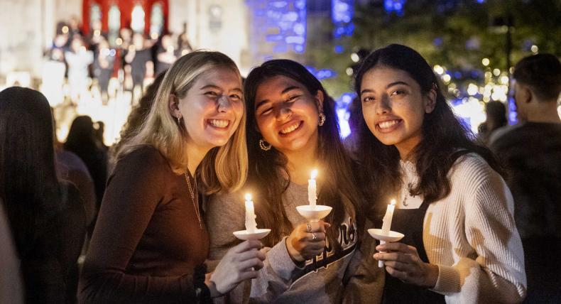 Three students stand in front of Main Building holding candles during Festival of Lights.