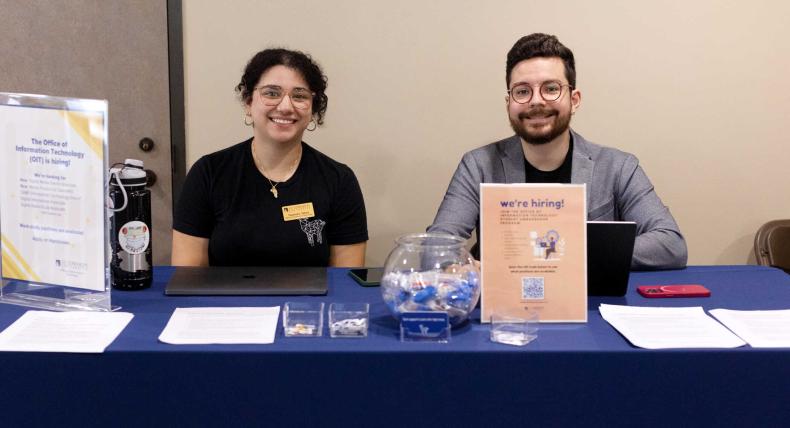 Two OIT staff members sit at a table during an event.