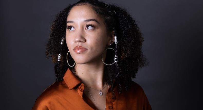 Alexis Reed wears a satin orange shirt and looks over her shoulder.