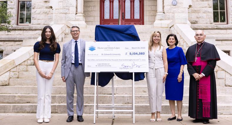 Five people stand with a large check on a stand at the steps of Main Building with the red doors in the background.