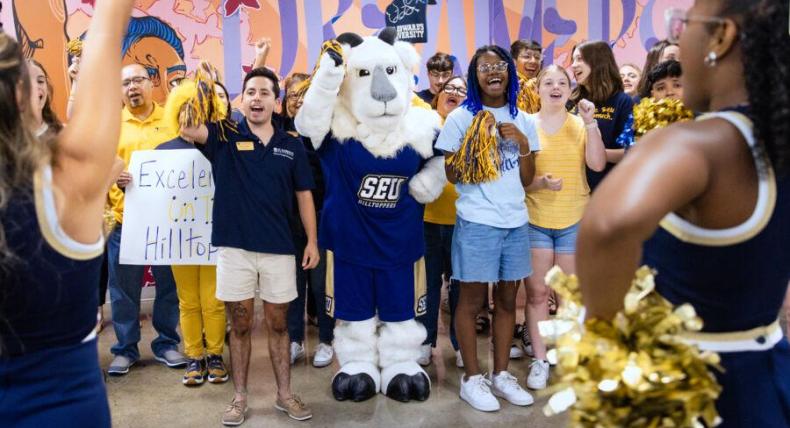 Cheerleaders frame a group of students and the Topper mascot as everyone cheers.