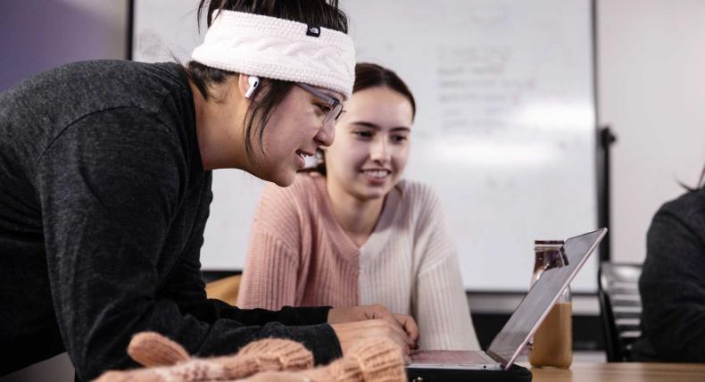 A student types on a computer as another student looks on.