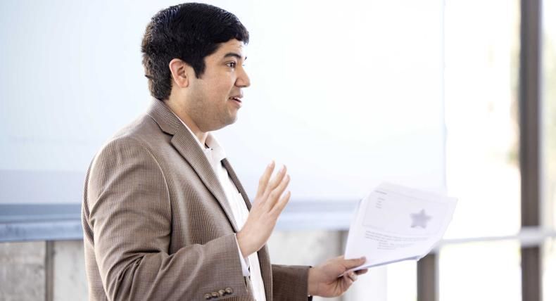 A person wearing a blazer holds papers and presents information.