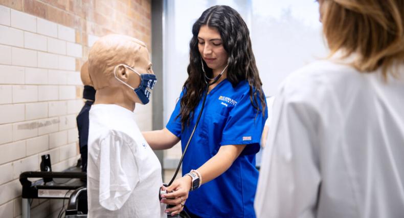 nursing student in blue scrubs learning in a nursing lab 