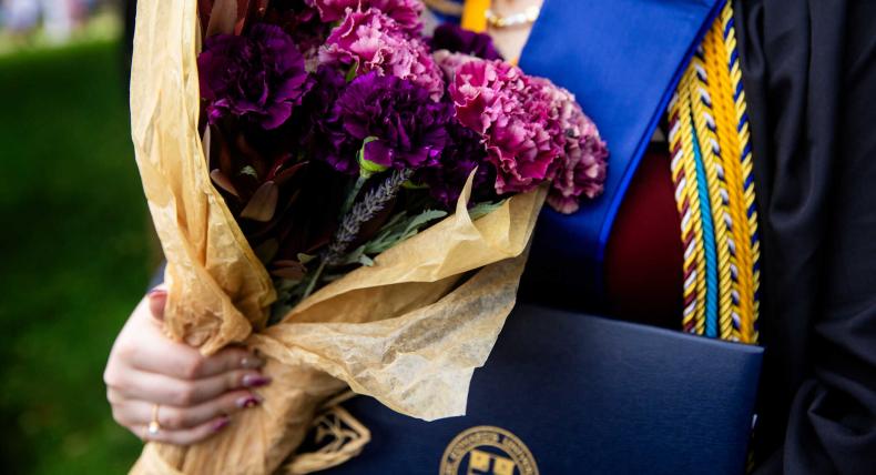 A detail of a graduate holding flowers and their degree.