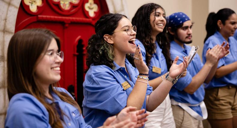 Five orientation leaders stand in matching blue polos and clap.